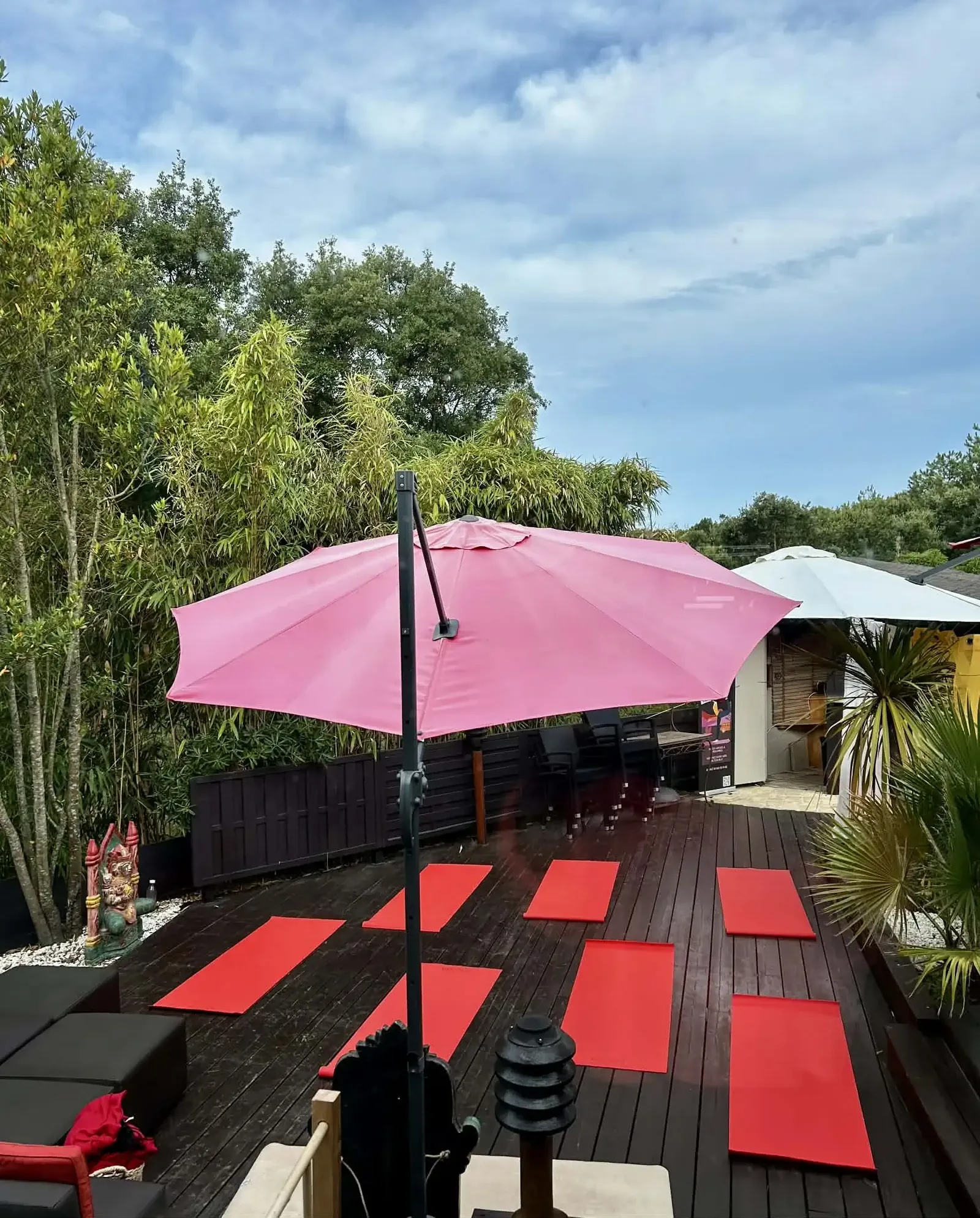 Vue plongeante de la terrasse en bois où se déroulent les cours de yoga à Moliets-et-Maa, tapis rouges installés sous le parasol